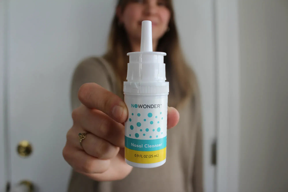 Person holding a NoWonder nasal cleaner bottle in front of a blurred background